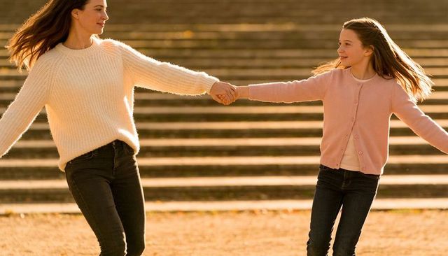 Mother and daughter holding hands on sunlit steps wearing knit sweater and cardigan
