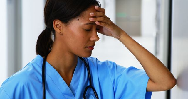 A young Asian female nurse appears stressed or fatigued, with copy space. Her expression and body language suggest she may be dealing with a challenging situation or long hours at work.
