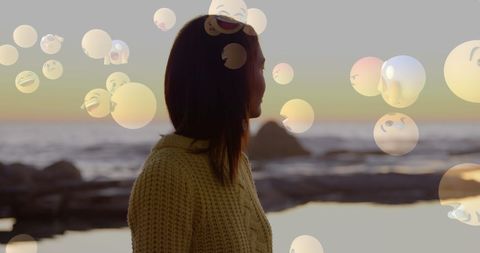 Woman on beach surrounded by floating emojis at sunset