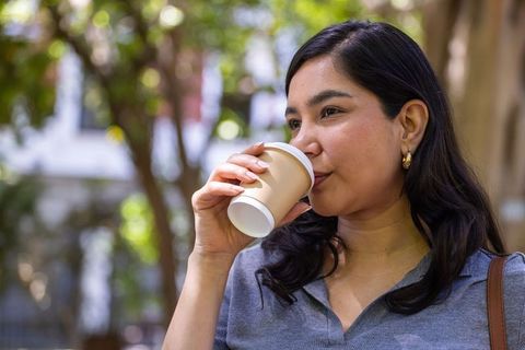 Urban woman sipping takeaway coffee outdoors with gold hoop earrings, casual grey top