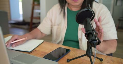 Mature woman podcasting from home recording with condenser microphone, laptop, notebook