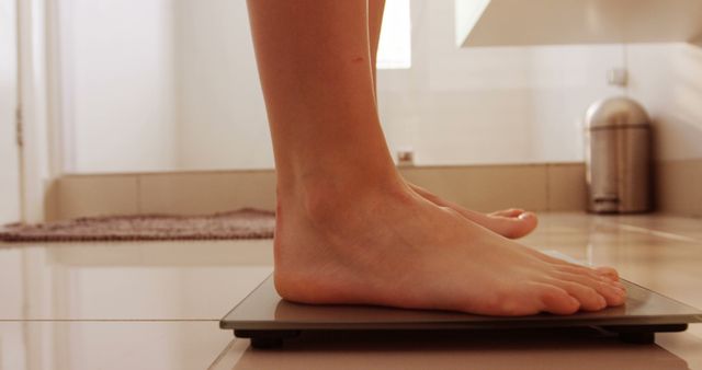 Close-up of person’s bare feet standing on a digital bathroom scale. This photo is ideal for articles or materials related to health, fitness, weight management, and personal wellness. Useful for promoting healthy lifestyle routines and diet plans, or illustrating concepts of weight tracking and progress in fitness regimes.
