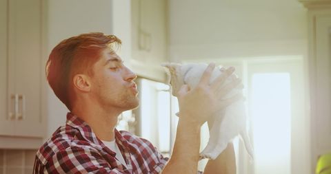 Man Affectionately Holding and Kissing Small Dog in Sunlit Kitchen