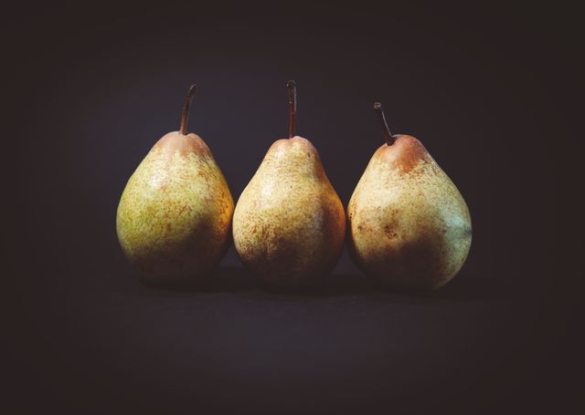 Three fresh pears standing in a row against a dark black background. Perfect for use in culinary blogs, health and nutrition articles, fruit product marketing material, and kitchen decoration.