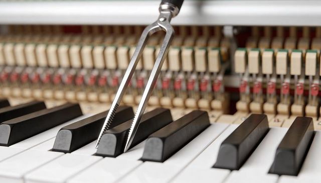 Close-up tuning fork touching piano key with exposed action mechanism for piano tuning