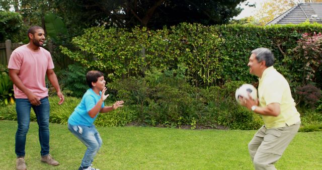 Three generations of men are enjoying a game of soccer in a green backyard. A grandfather, father, and son are bonding through the sport, creating a scene of happiness and togetherness. Ideal for advertisements promoting family activities, health and fitness, or outdoor entertainment. It can also be used in material highlighting the importance of family time and multigenerational relationships.