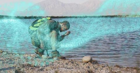 Hiker Scooping Water from Lakeshore with Scenic Mountain View