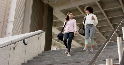 Young Women Walking Down Campus Stairs Carrying Duffel Bags Conversing After Workout Urban