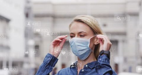 Young woman adjusting surgical mask with smartwatch and social media overlay in city plaza
