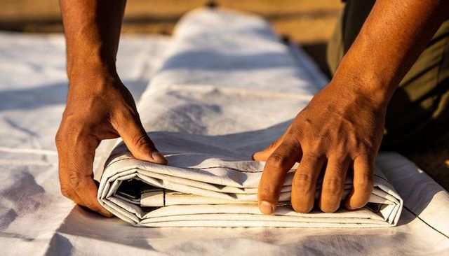 Artisan hands folding heavy canvas in warm sunlight showing outdoor textile craftsmanship