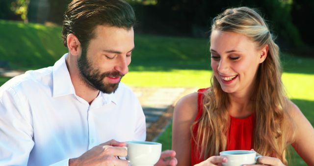 A Caucasian man and woman enjoy a conversation over coffee outdoors, with copy space. Their relaxed demeanor and smiles suggest a casual, friendly meeting or a date in a pleasant setting.