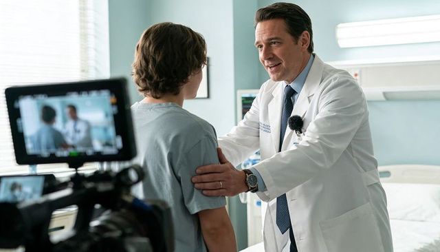 Doctor reassuring teenage patient in hospital room with camera rig filming medical scene