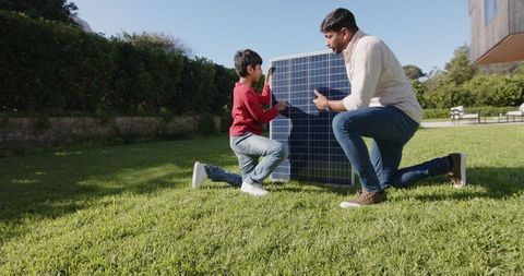 Father and Son Working with Solar Panel on Lawn During Sunny Day