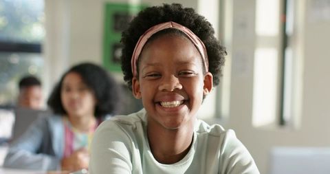 Smiling schoolgirl wearing headband sitting in bright classroom learning and engaging