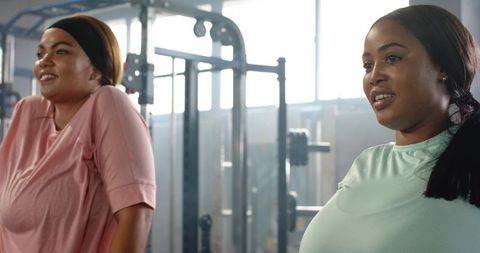 Two women working out leaning on cable machine in gym friendly strength training moment