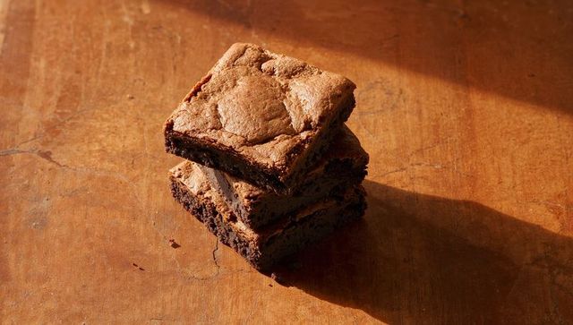 Sunlit Stack of Fudgy Chocolate Brownies on Rustic Wooden Tabletop with Crumbs and Shadow