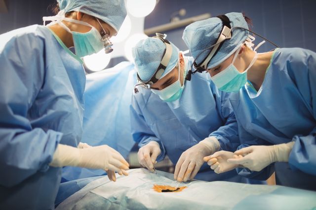 Depicts a team of surgeons performing a surgical operation in a hospital's operating room. Ideal for use in healthcare-related articles, medical presentations, educational materials, and advertisements for medical services.