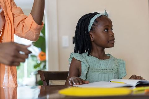 African american mother helping school-aged daughter with homework at bright home table