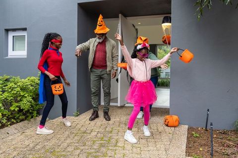 African American family celebrating Halloween with kids in colorful costumes on porch