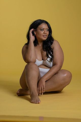 Curvy model embracing body positivity in white lingerie sitting on yellow backdrop
