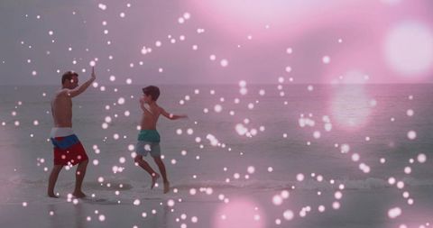 Shirtless father and son running on shoreline with pink bokeh, summer family bonding