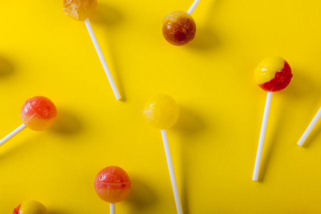 Directly above close-up view of lollipops against yellow background. unaltered, unhealthy eating and sweet food concept.