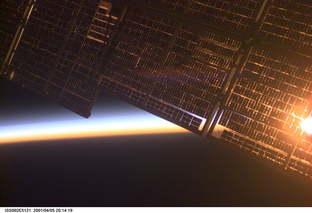 This image depicts the solar panel of the Zvezda Service Module on the International Space Station set against Earth's horizon at dawn. It was captured by an Expedition Two crew member in 2001. This image can be used in publications and media related to space exploration, technological advancements in space, educational resources, and materials highlighting views from the ISS.