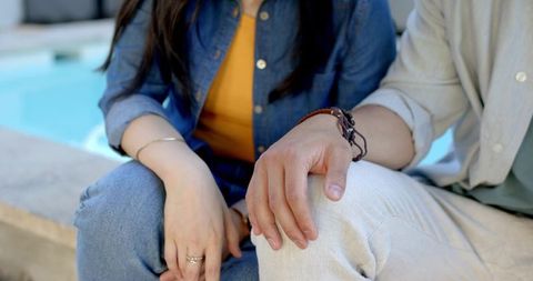 Asian couple sitting by pool wearing denim and casual jewelry showing relaxed companionship