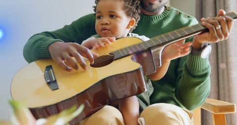 Father teaching baby guitar during cozy home bonding session