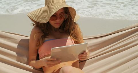 Woman Relaxing in Hammock on Beach with Digital Tablet