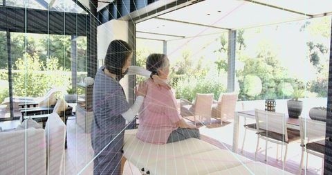 Caregiver massaging senior woman on treatment bench in bright modern home with glass walls