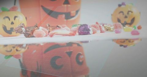Pastel halloween candy and jack-o-lantern buckets reflecting on glossy surface studio arrangement