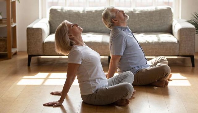 Senior couple practicing seated backbend in sunlit living room boosting mobility and wellbeing
