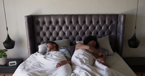 Couple sleeping back-to-back on king bed with tufted headboard and bedside smartphone