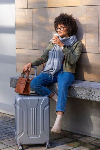 Relaxed urban traveler enjoying coffee while waiting with suitcase and leather handbag