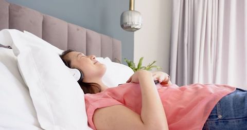 Woman Relaxing on Bed with Headphones and Smartphone