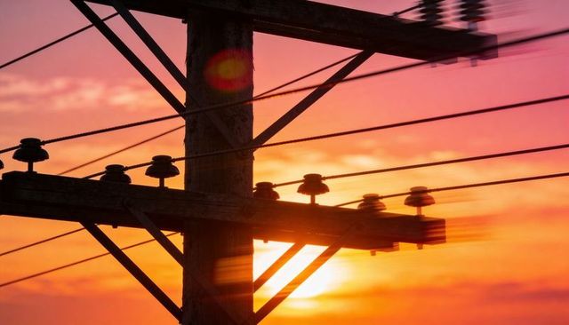 Wooden utility pole silhouetting against vibrant sunset with lens flare and power lines