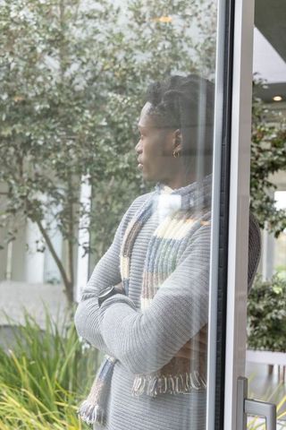 African-american man standing and looking through glass door in modern lobby with courtyard greenery