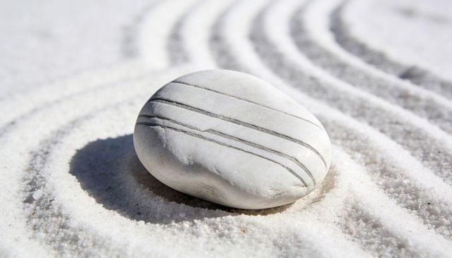 Striped white pebble resting on raked sand with curved grooves and soft shadow