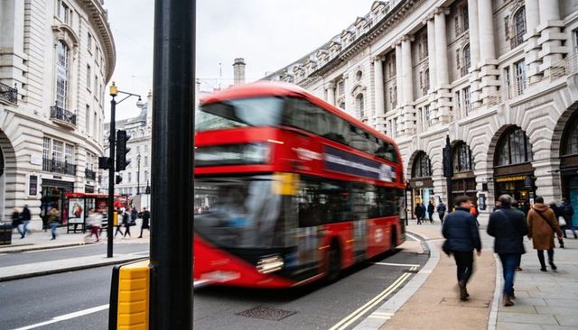 Turning red double-decker bus blurring along curved london street with historic architecture