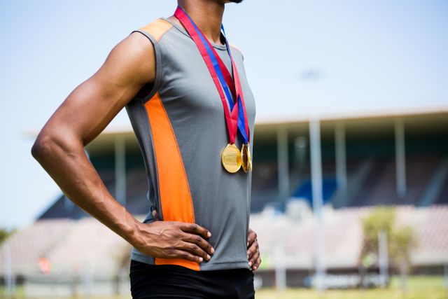 Mid section of athlete posing with gold medals around his neck in stadium