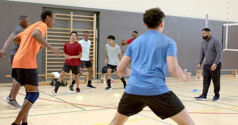 Diverse male volleyball team practicing fast-paced court drills with coach and cones