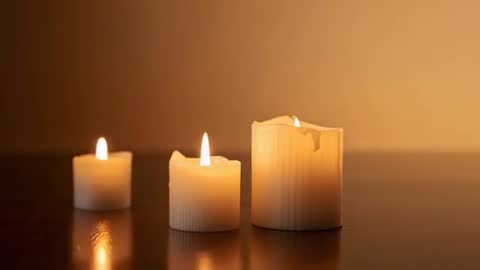 Three Burning Pillar Candles Flickering with Melting Wax and Warm Tabletop Reflection