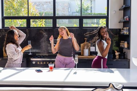 Three african-american women dancing and laughing in sunlit contemporary kitchen