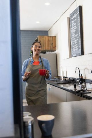 Smiling african american barista holding red mug behind modern minimalist cafe counter