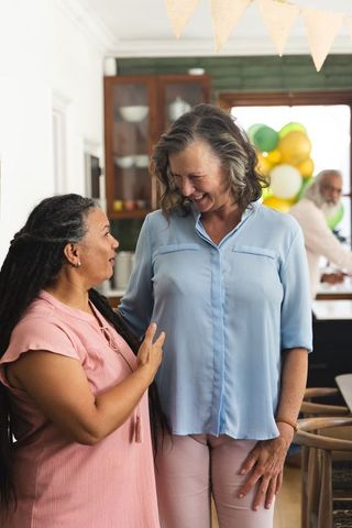 Middle-aged friends celebrating at home kitchen party smiling and chatting near balloons