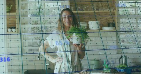 Smiling woman holding potted herb in bright rustic kitchen with blue ar data grid overlay
