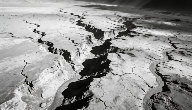 Aerial black-and-white canyon landscape cutting cracked desert plateau with deep ravines