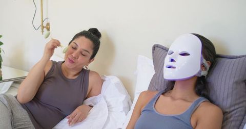 Diverse friends relaxing with led light therapy mask and jade roller for at-home skincare