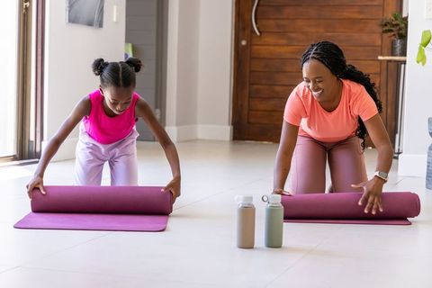 African mother and daughter unrolling purple yoga mats in sunlit home preparing workout